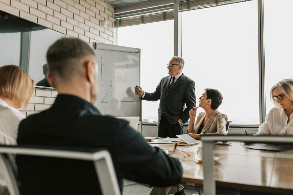 Business leader presenting growth strategies on a whiteboard to colleagues during a meeting.